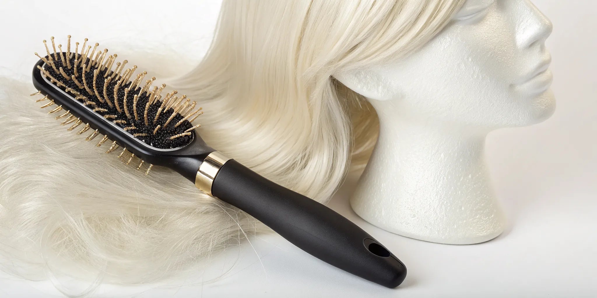 A specialized wig brush with looped bristles resting on a blonde wig.